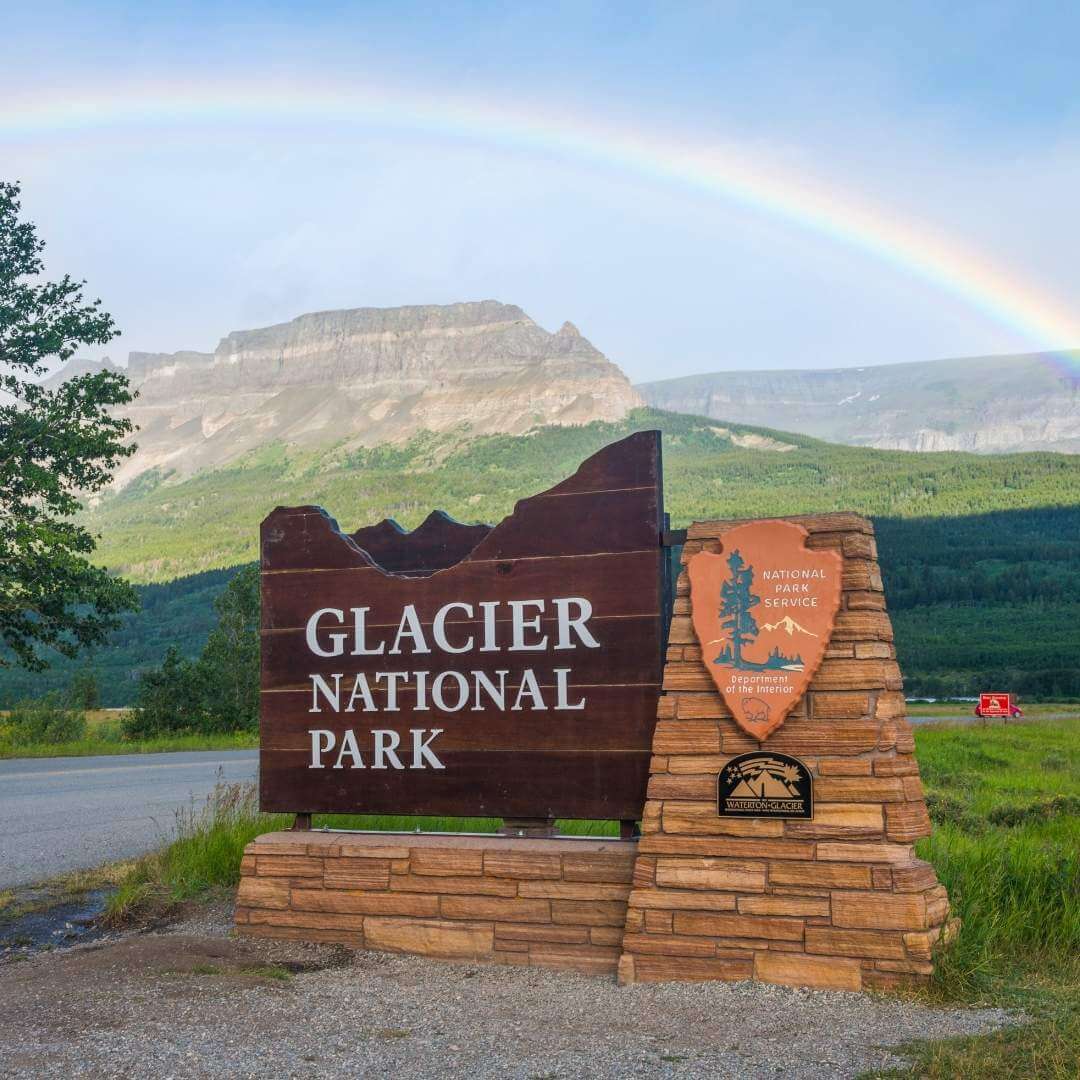 Glacier National Park sign with a rainbow in the background